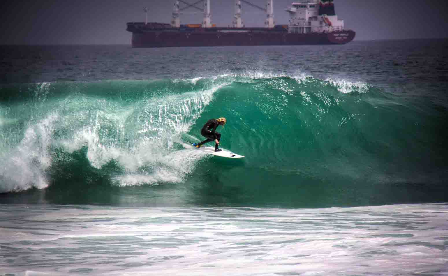 Surfer carving a green wave with a bulk cargo ship parked behind
