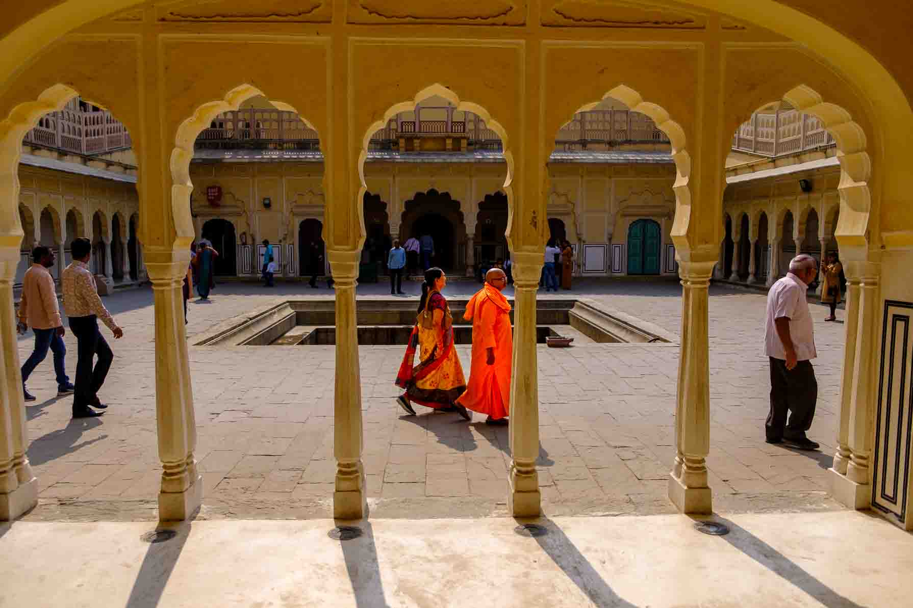 Gilded finials over a palace courtyard where a woman crosses with a basket on her head