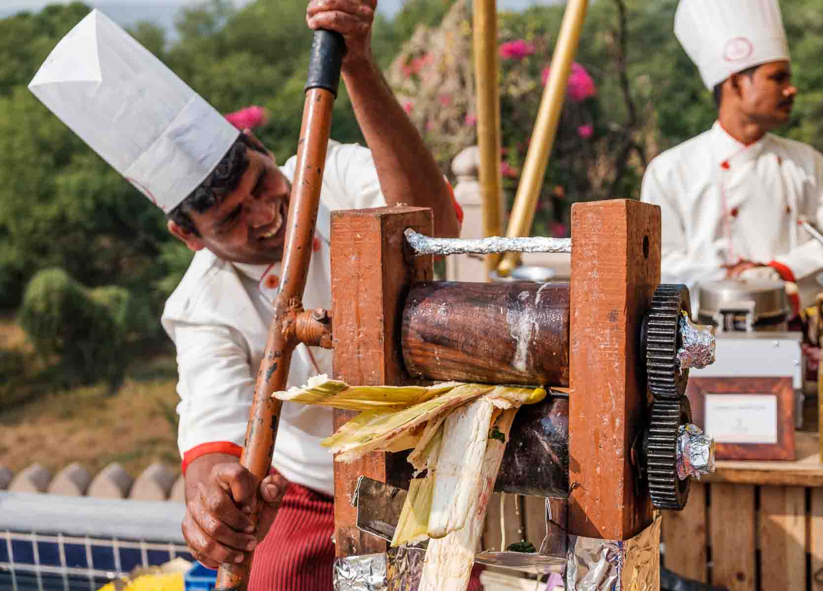 Tall-hatted attendant pressing sugarcane juice at a ceremonial station