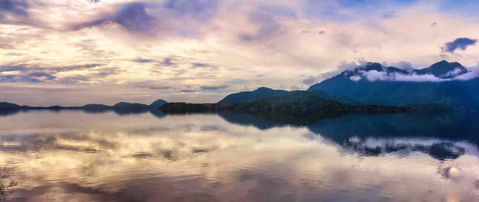 A still lake mirroring cloud-wrapped mountains at dusk