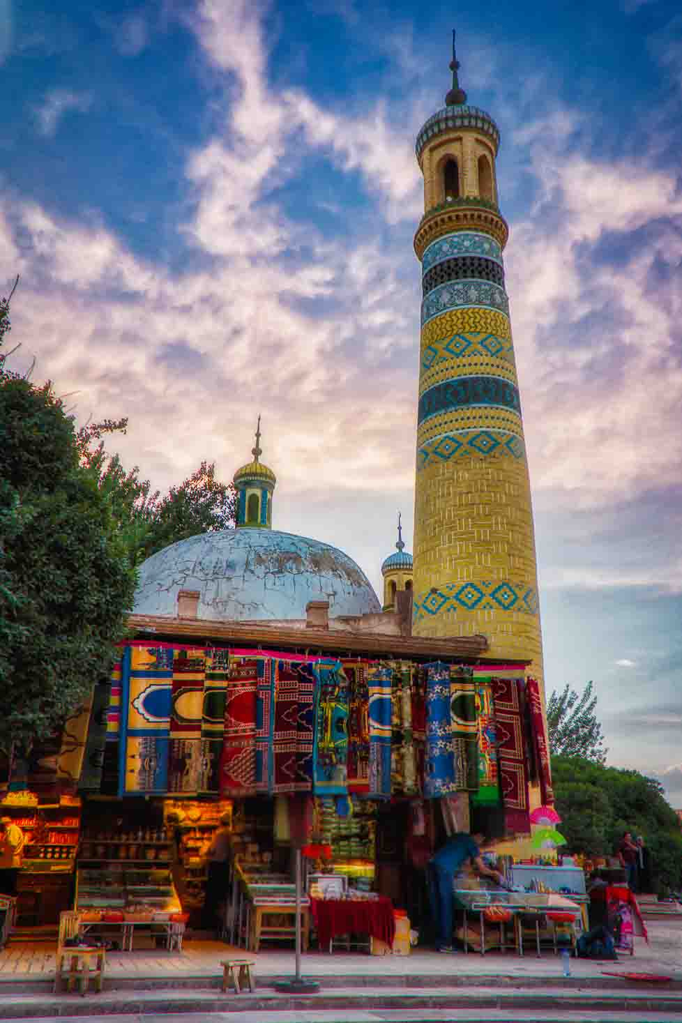 Uyghur mosque with a patterned minaret rising above the bazaar at dusk