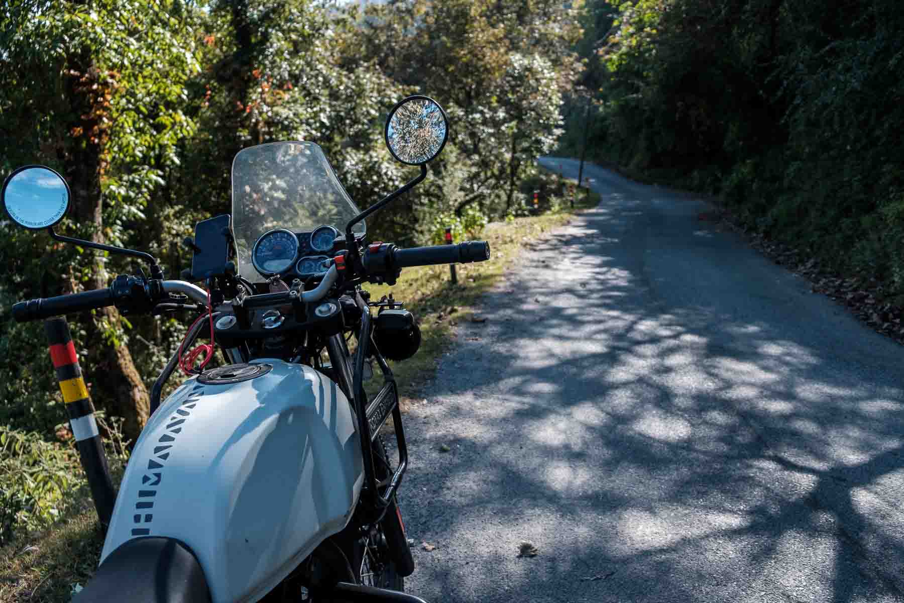 Royal Enfield handlebars and dashboard on a dappled mountain road