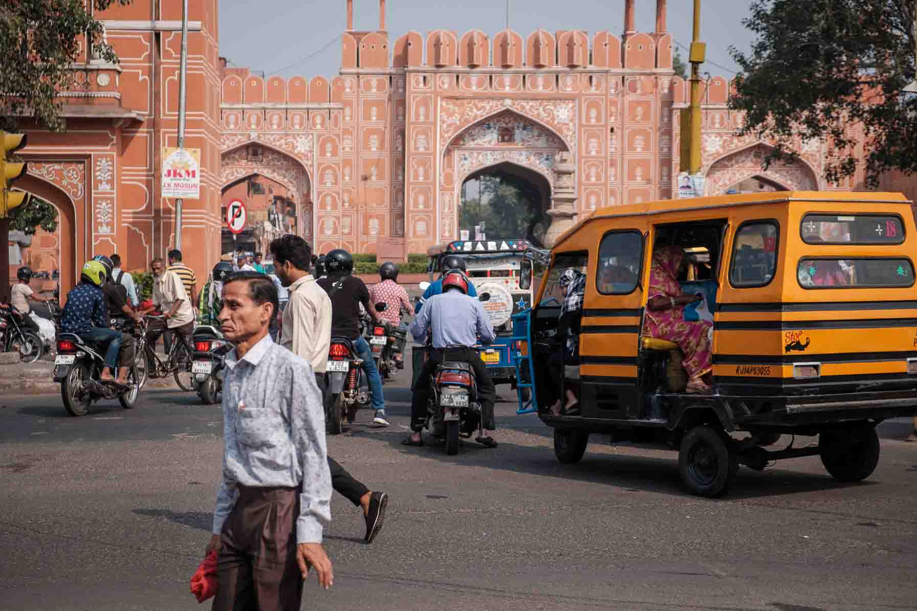 Yellow auto-rickshaw and motorbikes funneling toward a pink city gate