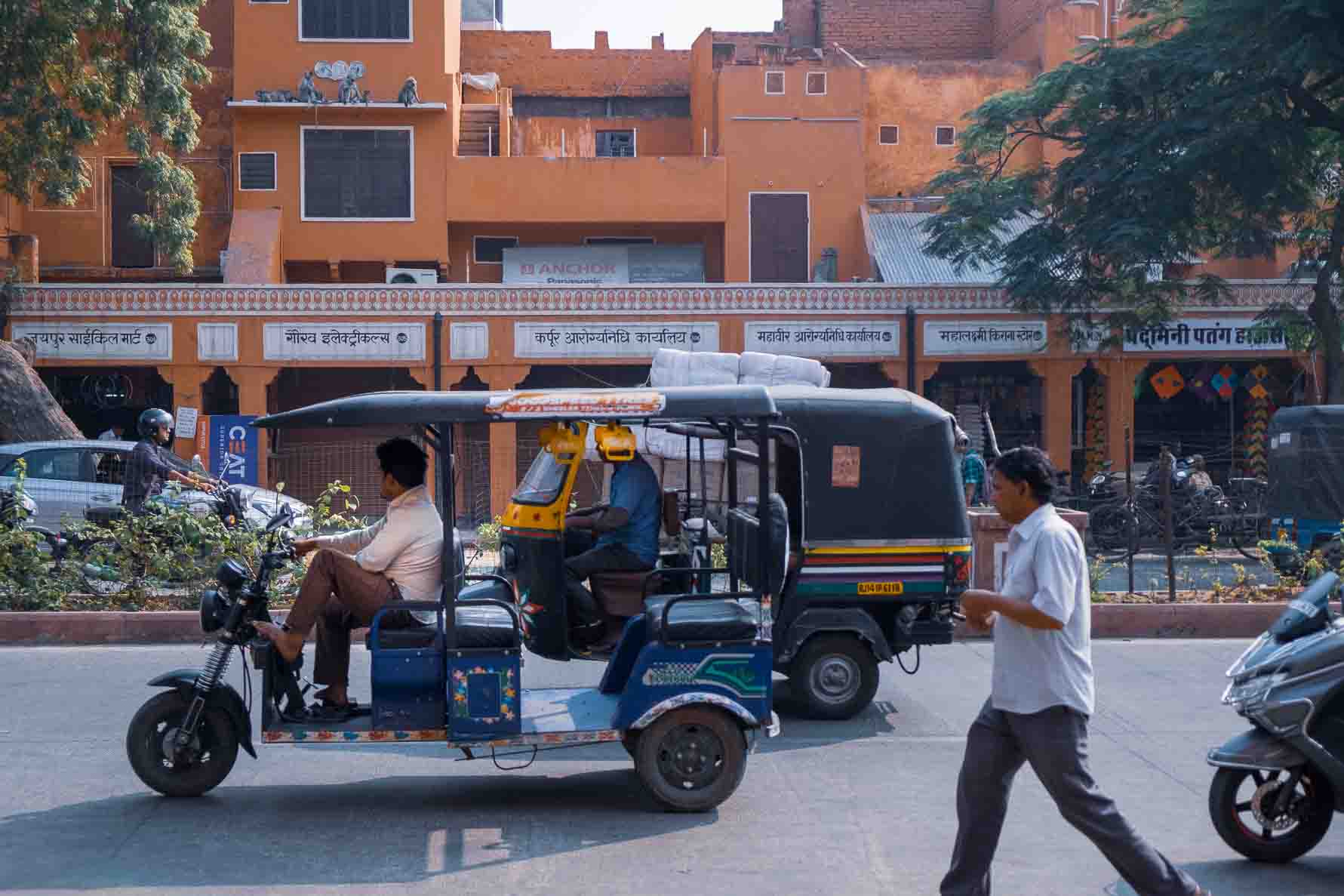 Blue and yellow auto-rickshaws idling roadside, passenger checking a phone
