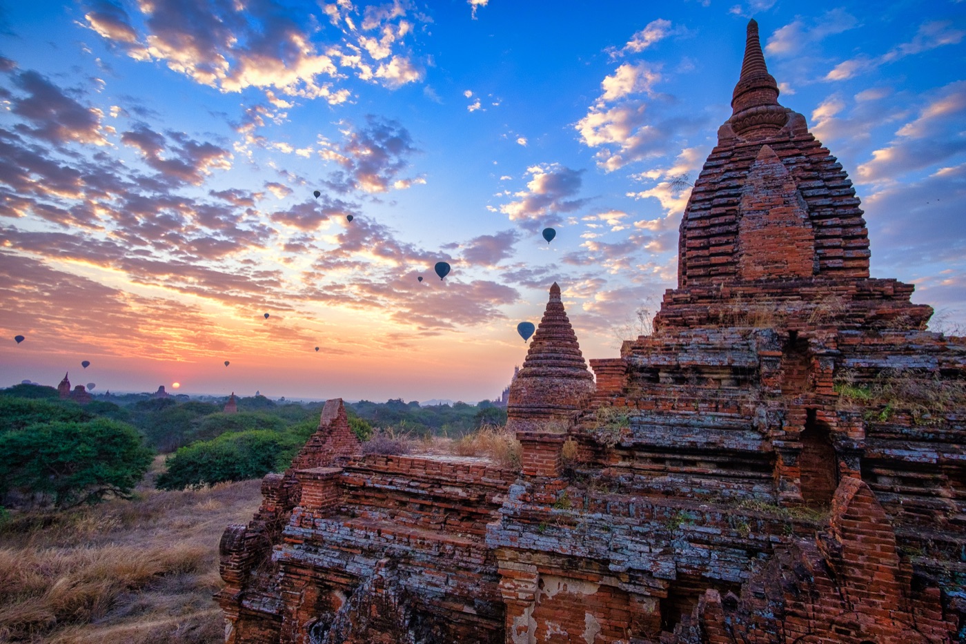 Brick temples of Bagan standing above the treeline under a broad clouded sky.